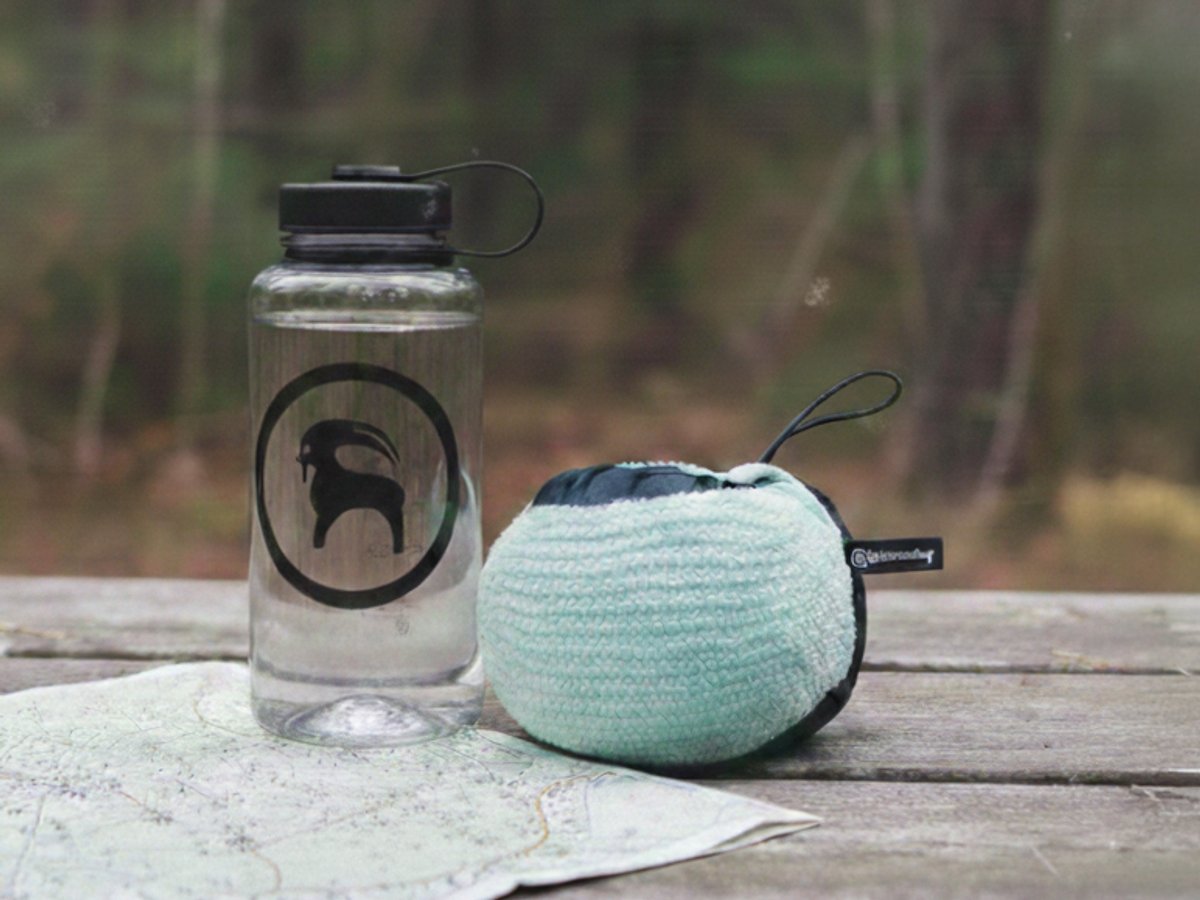 Fleece jacket packed into stow pocket with elastic cinch drawn tight and carry tab showing next to a water bottle on a picnic table.