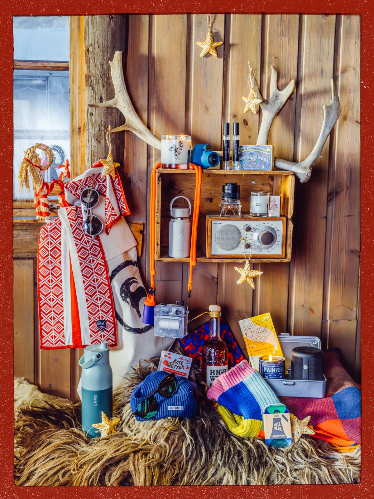 Holiday gift display of small gifts, including a radio, candles, water bottles, a beanie, and sunglasses, in a rustic cabin.