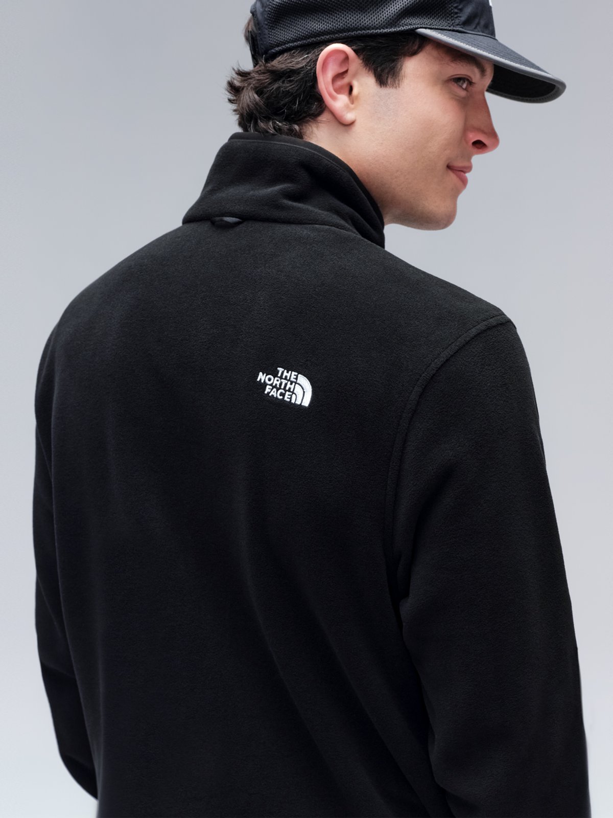 A man wears a black The North Face fleece, facing away and looking over his shoulder.