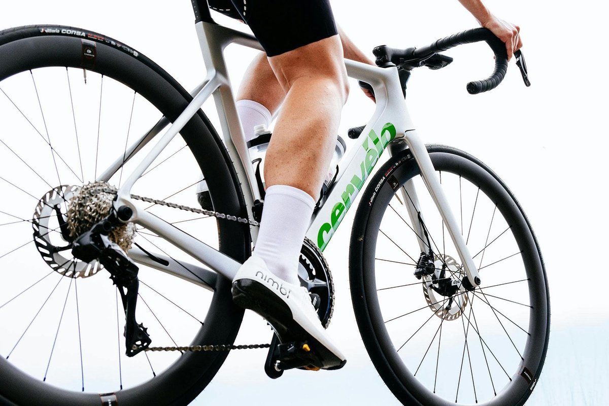 Road cyclist wearing Nimbl cycling shoes and white socks seated on Cervélo carbon road bike with Vittoria Corsa tires and disc brakes