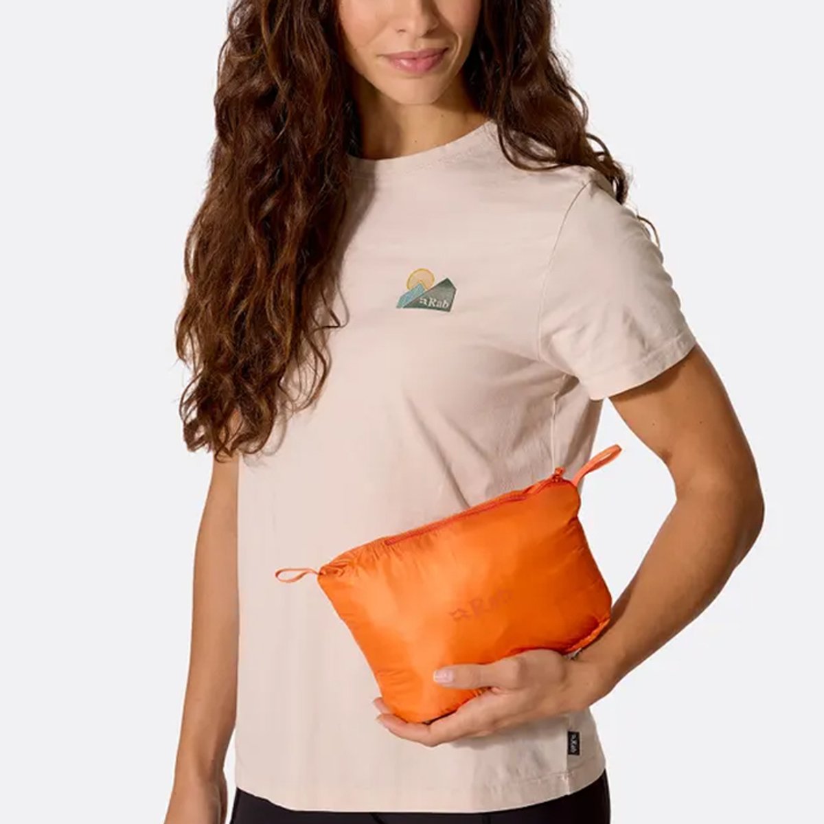 A woman holds a Rab jacket folded into a storage zip case.