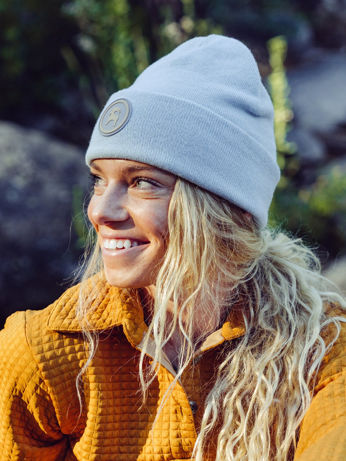 A woman with long curly blonde hair is wearing a folded beanie with a round goat patch.