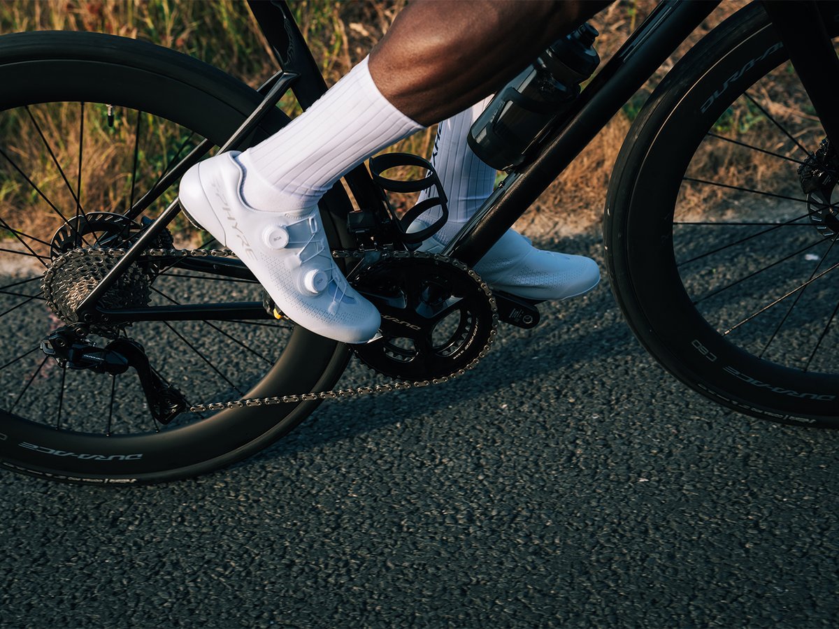 Top-down view of a white S-PHYRE shoe mid-pedal-stroke, upper clearly visible, Dura-Ace crank and chain in frame