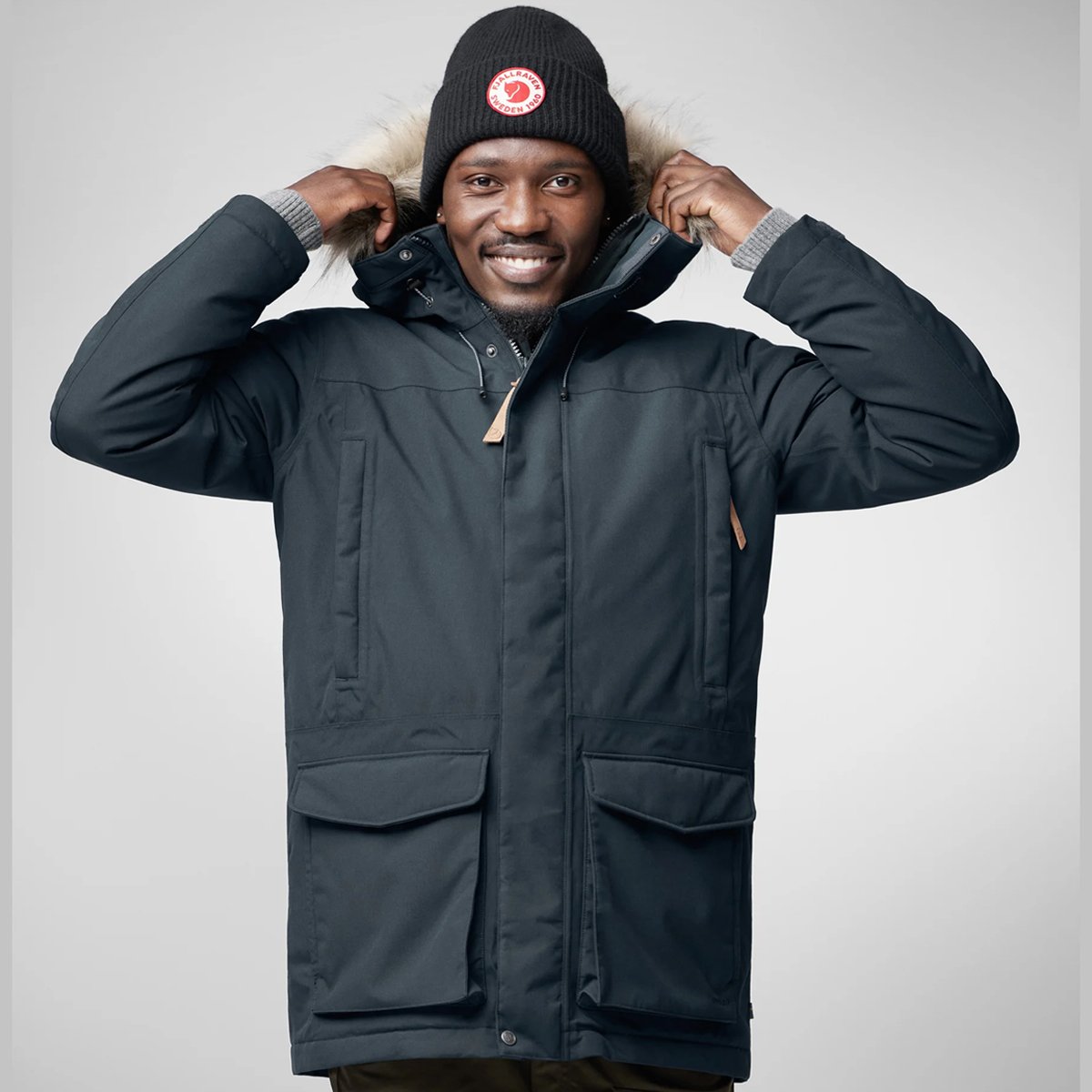 A man wears a Fjallraven beanie and Nuuk parka, smiling.
