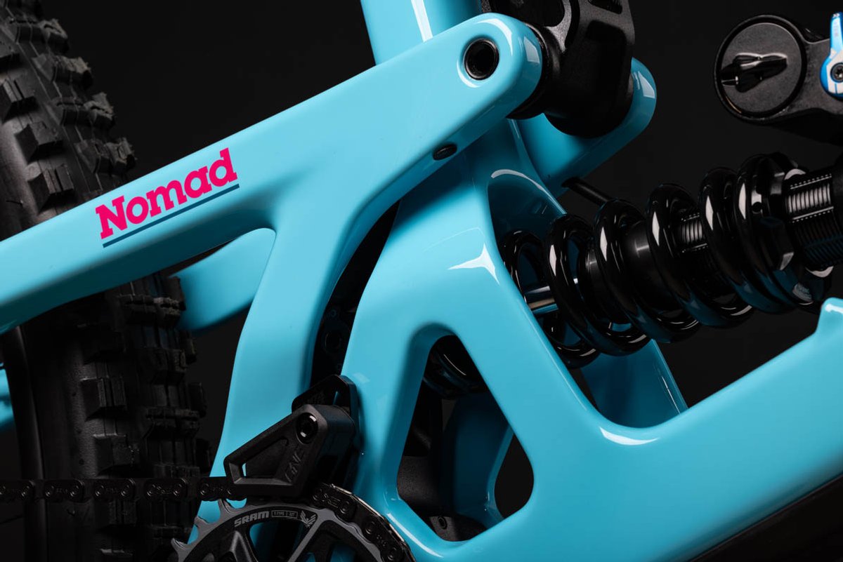 Close-up of teal Santa Cruz Nomad full-suspension mountain bike rear triangle coil shock and carbon frame junction detail