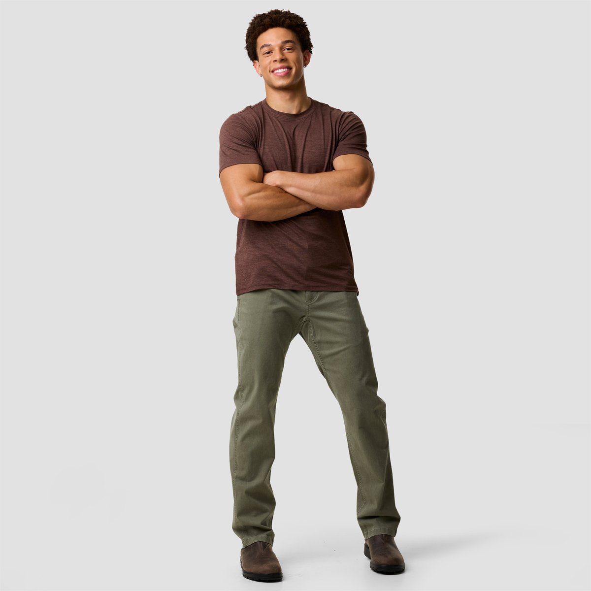 Man wearing brown heathered crew neck t-shirt with BGA Venture Daily pant and brown suede boots standing against white background.