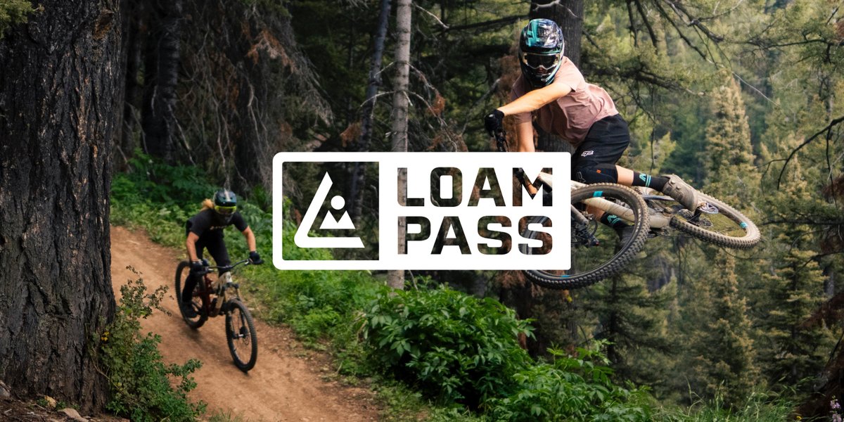 Mountain biker launching off a jump in a forested trail park, featuring the Loam Pass logo.