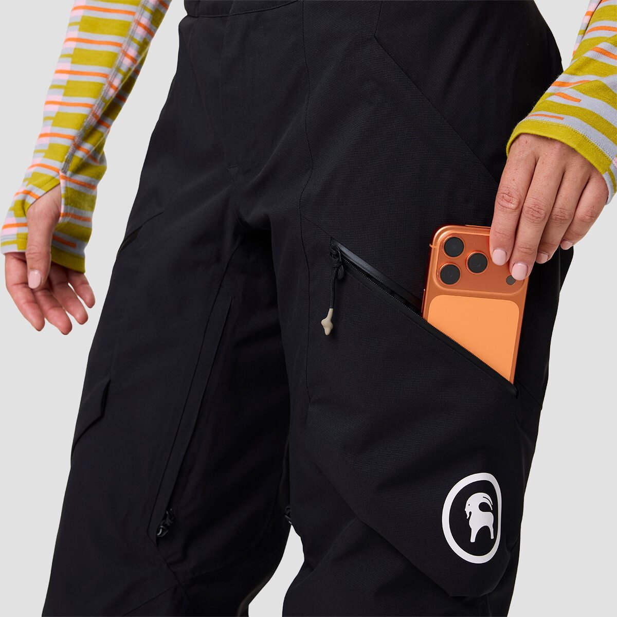 Person wearing Cottonwoods ski pant and placing phone in zippered thigh pocket.