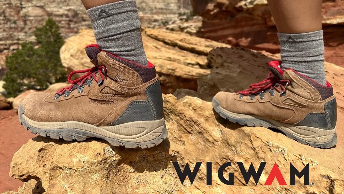 Hiker wearing tan and gray Wigwam hiking boots with red laces standing on rocky terrain in a desert landscape.