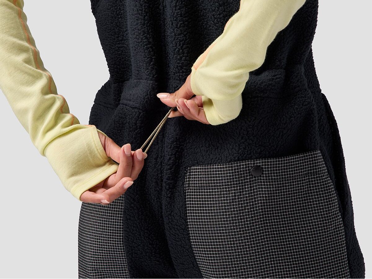 Close-up of a person cinching the waist of black fuzzy overalls from the back.