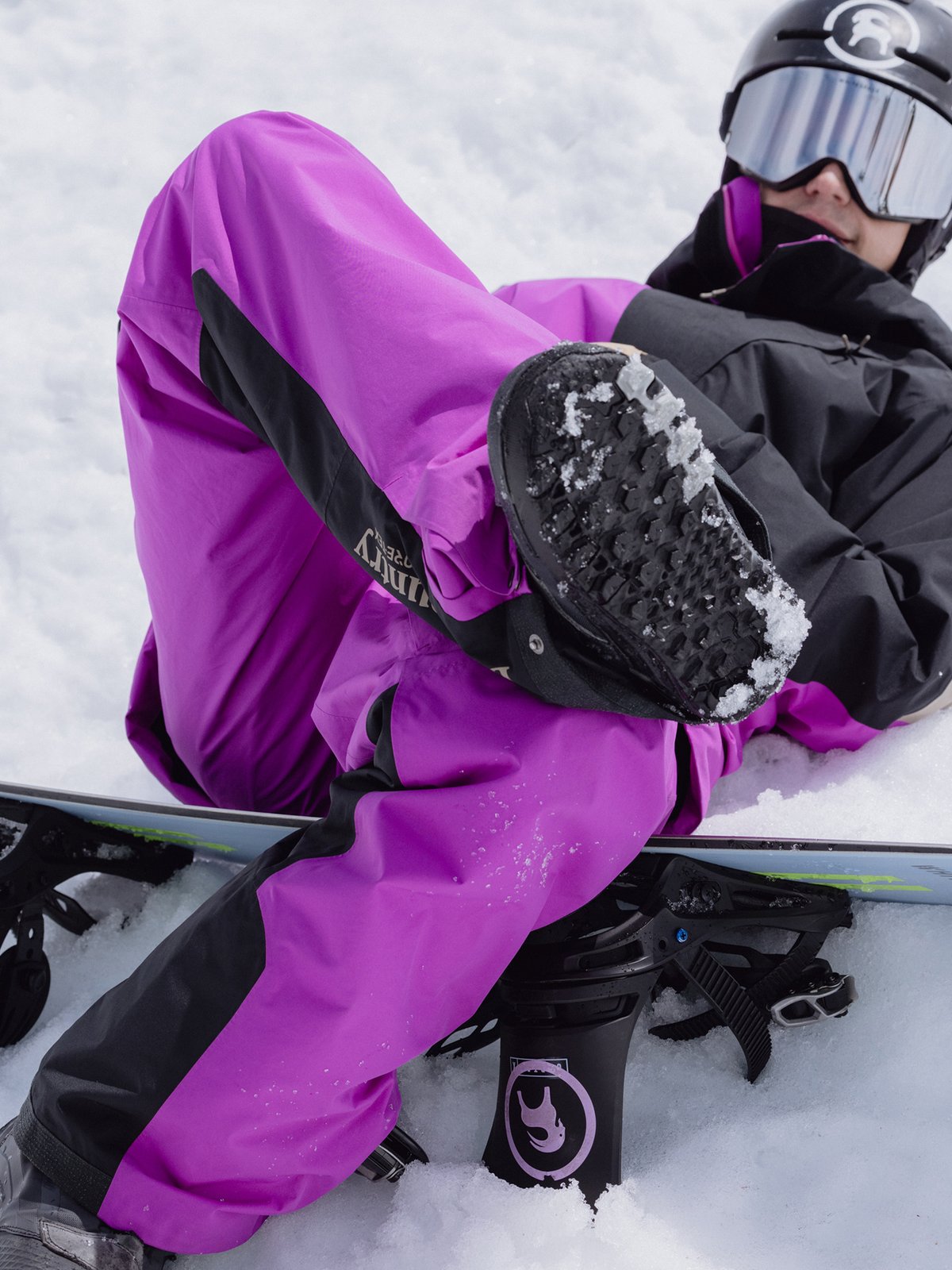 A snowboarder chills between runs, crossing one boot over his knee.