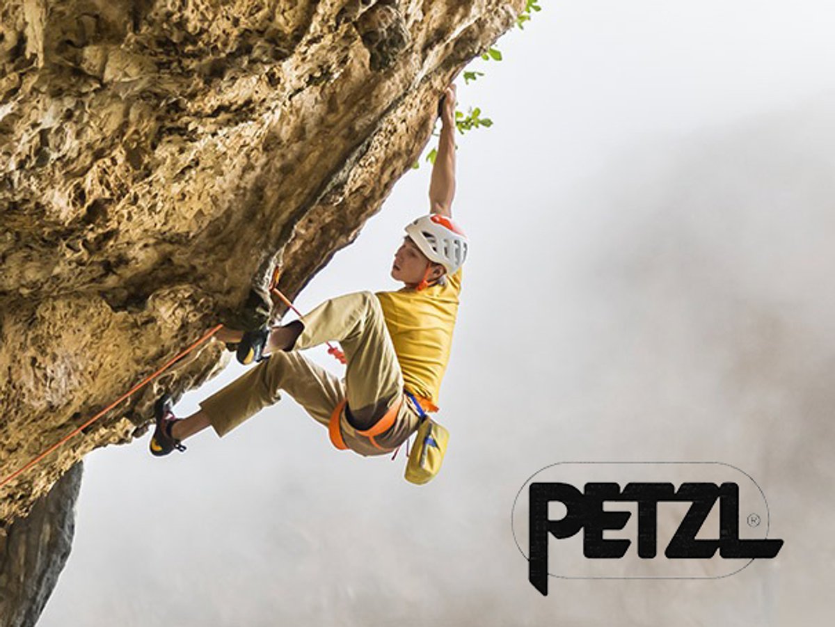 A rock climber in a yellow shirt and helmet hanging from an overhang on a limestone cliff; the Petzl logo is in the bottom right.