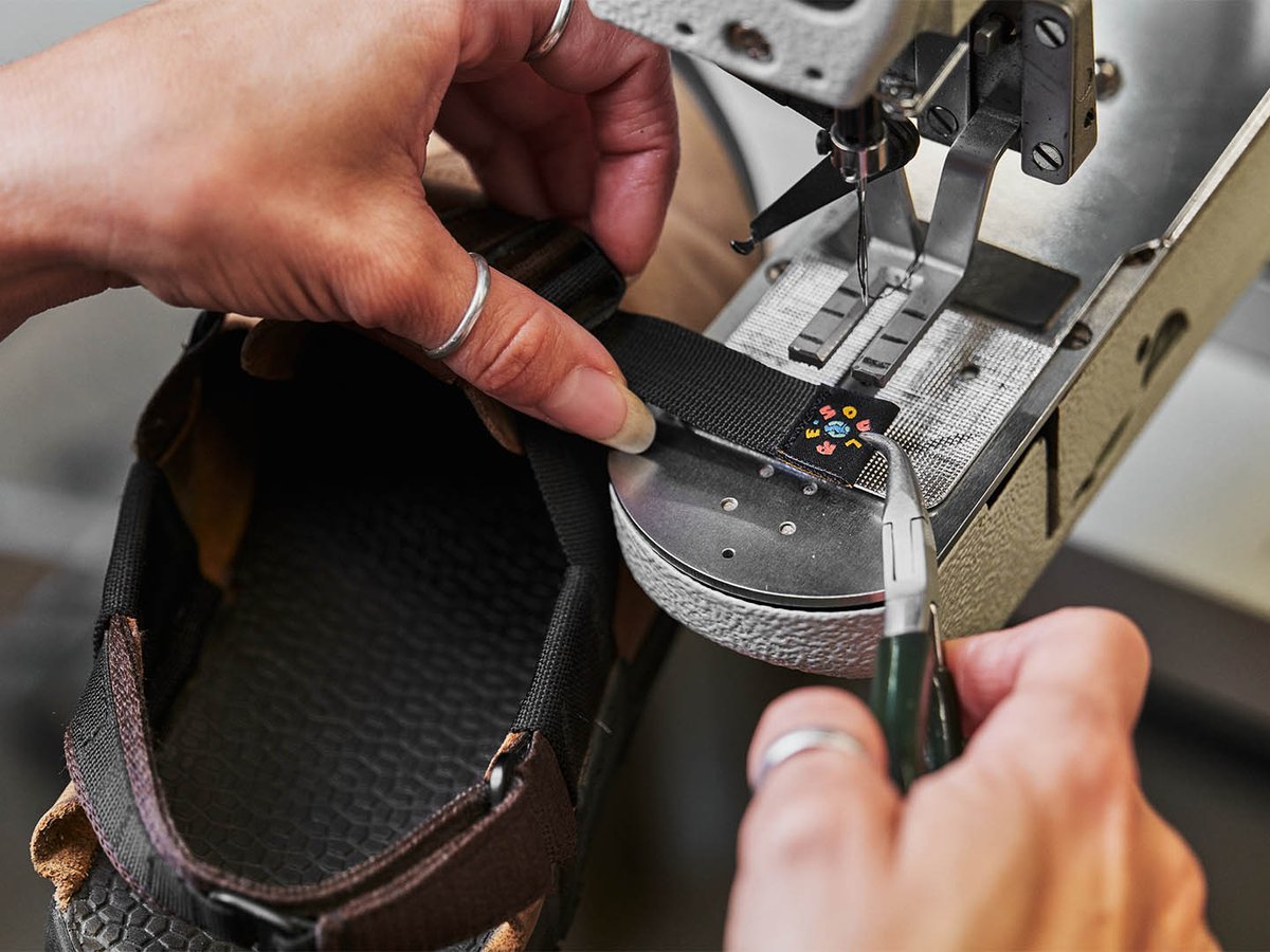 Close-up of hands feeding a Bedrock Mountain Clog through an industrial sewing machine during resole repair, showing footbed texture and Bedrock logo patch