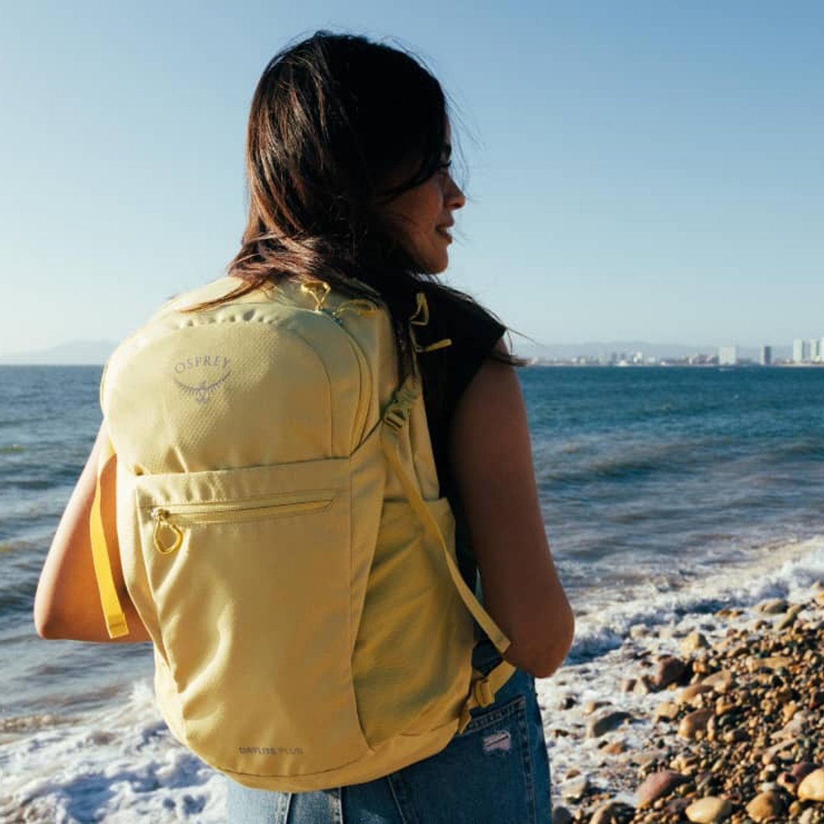 A woman wearing an Osprey Lifestyle pack looks out over the ocean.