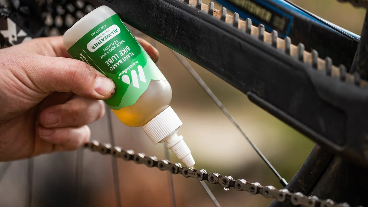 Person applying bike chain lube from a green squeeze bottle to a bicycle chain during maintenance.