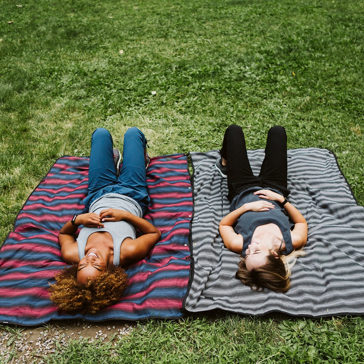 Two people laying on Coalatree Katchula blankets that are snapped together to make a large blanket in the grass. 