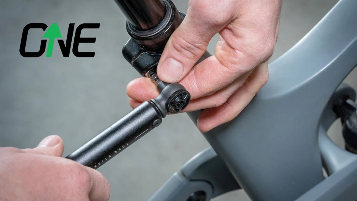Person adjusting a black bicycle seatpost clamp on a gray frame with the ONEUp brand logo visible in the upper left.