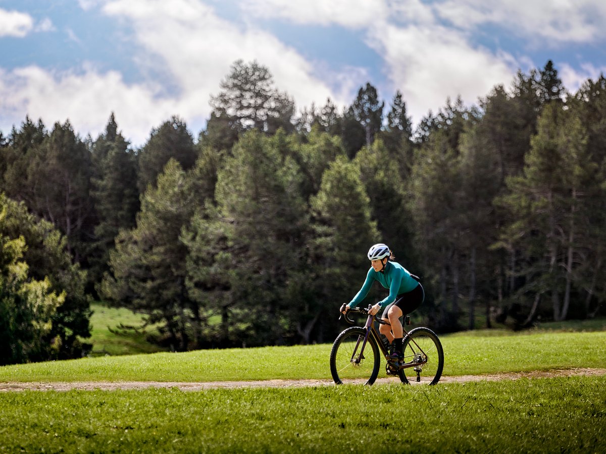 A woman rides a bike against a stunning backdrop of emerald green grass and pine trees.