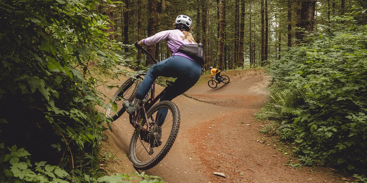 Two mountain bikers racing down a flow trail in the forest.