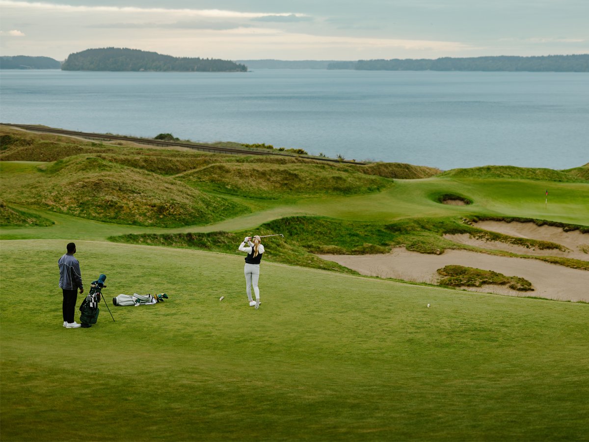 A woman tees off onto a golf course that overlooks a large body of water.