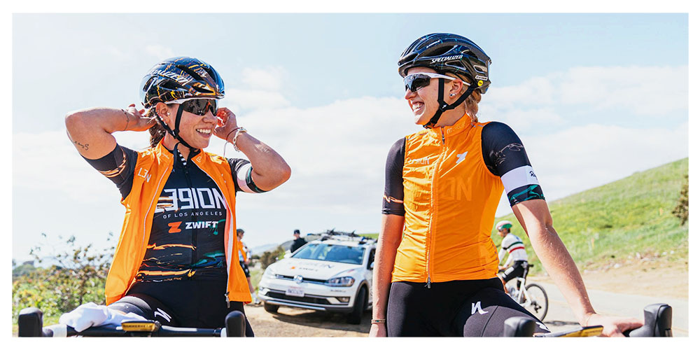 two Legion riders standing and talking, team car parked behind them